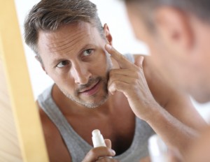 Man in bathroom applying cosmetics on his face